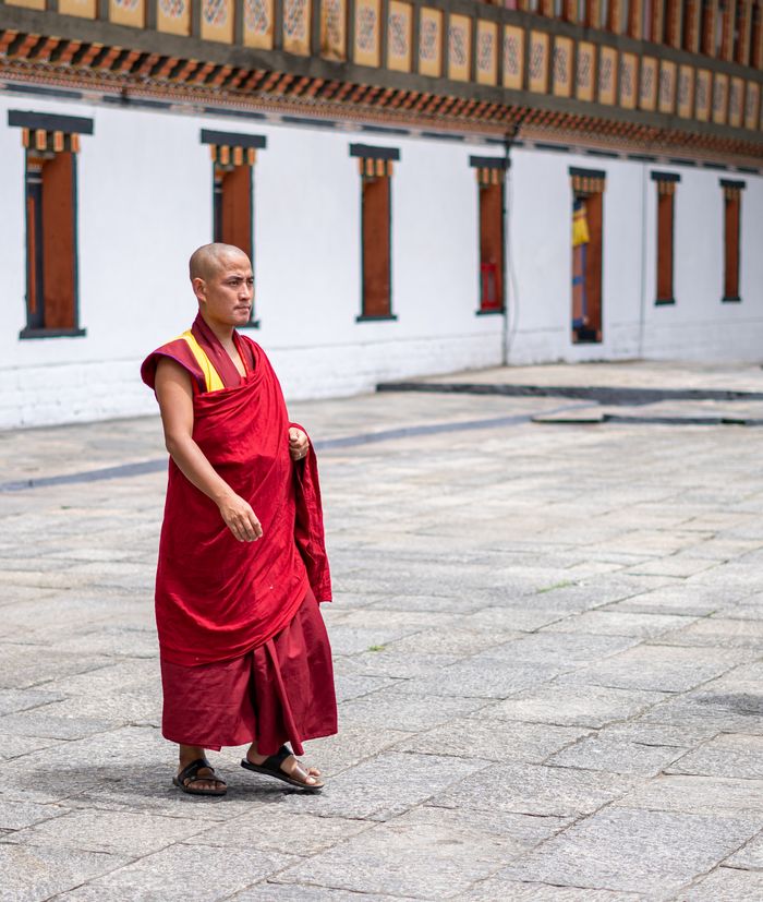 A Buddhist monk in red robes walking by a traditional Bhutanese temple, exemplifying peace and tradition.