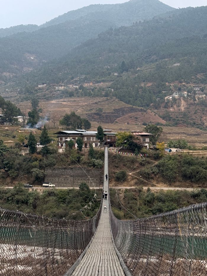 A picturesque suspension bridge surrounded by Bhutan's lush green mountains and charming houses.